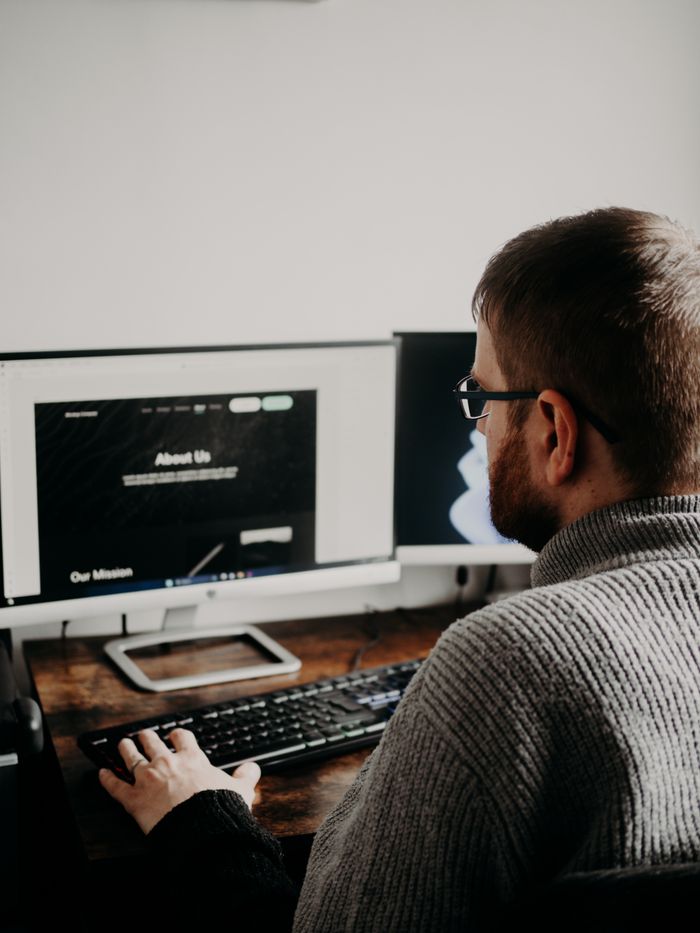 Un homme travaille sur la conception d’un site dans un bureau à domicile, installé devant deux écrans.